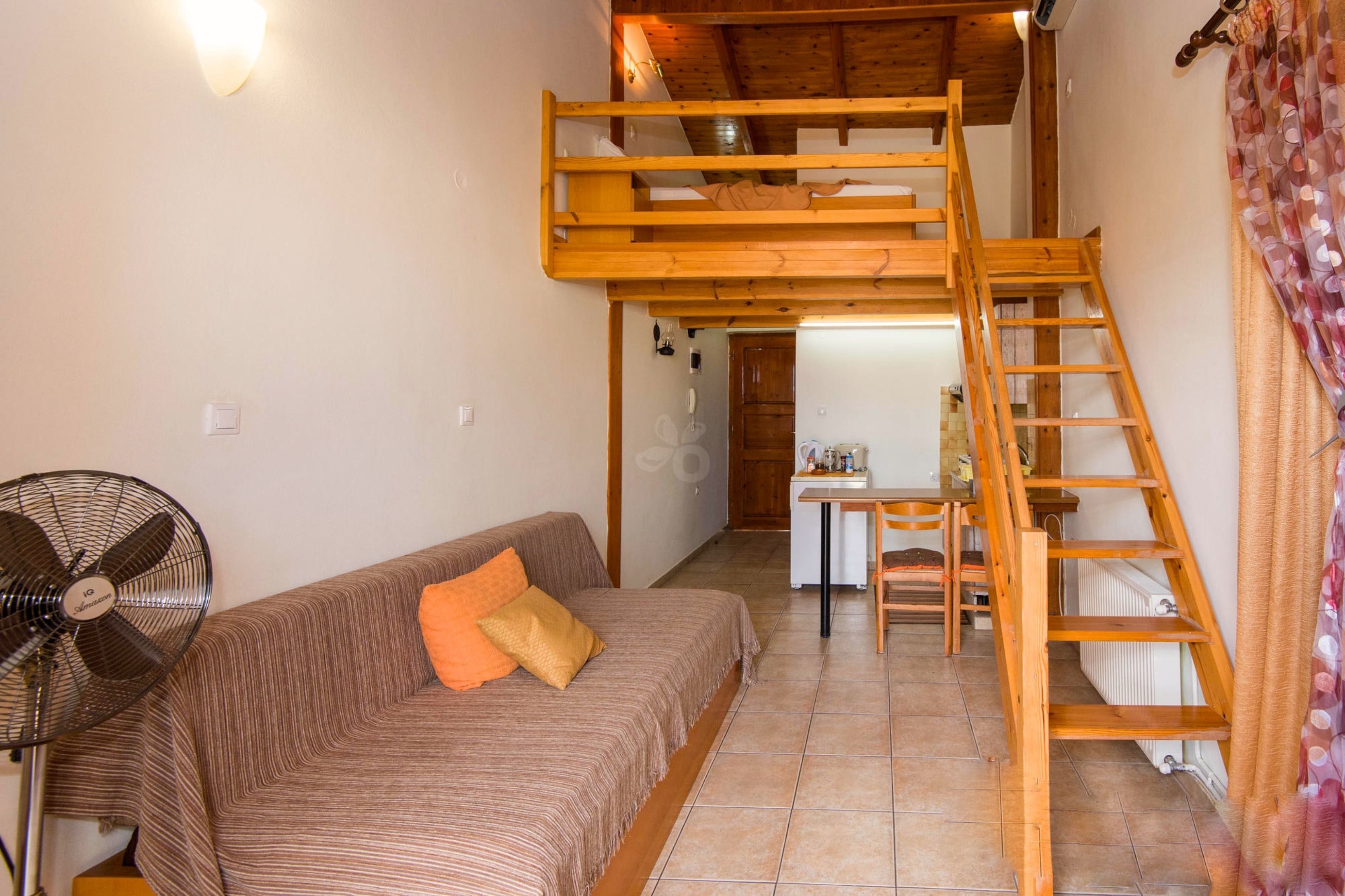 A room with a bunk bed, a sofa, a fan, and a table with chairs.
