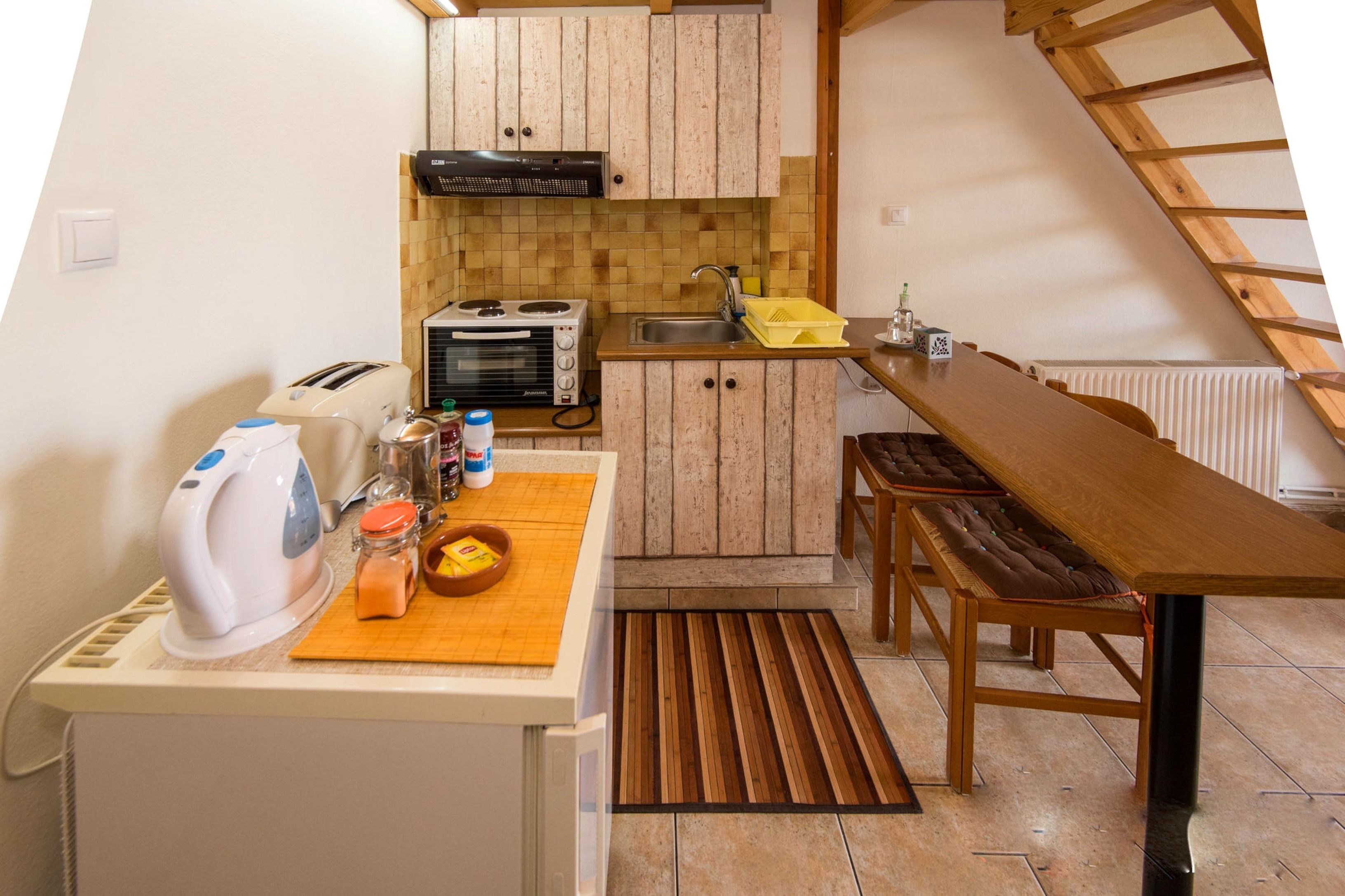 A compact kitchen with wooden cabinets, a stove, a sink, and a dining table with benches.