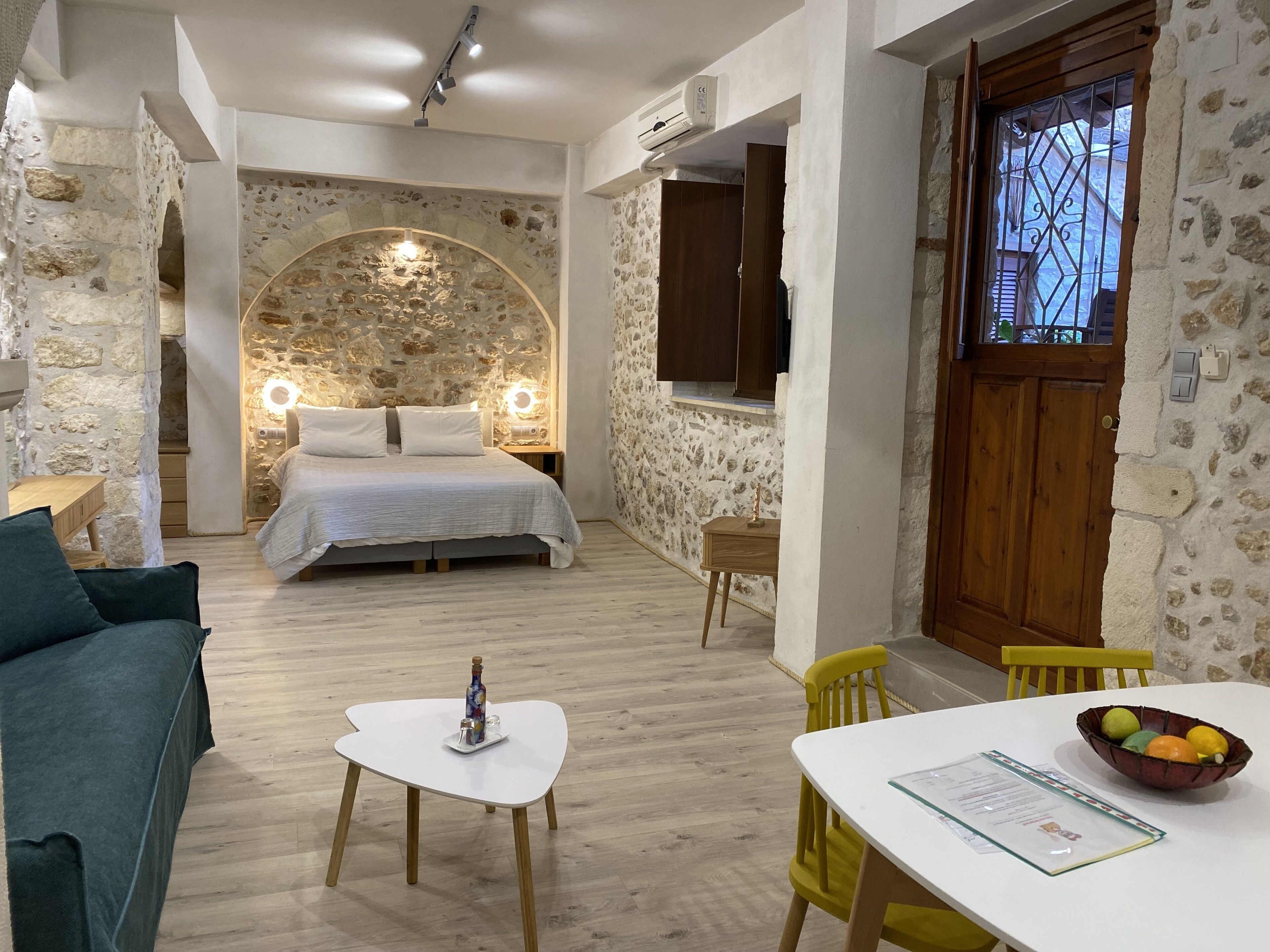 Un dormitorio acogedor con pared de piedra, una cama con ropa de cama blanca, una mesita de noche con lámpara y una puerta de madera.