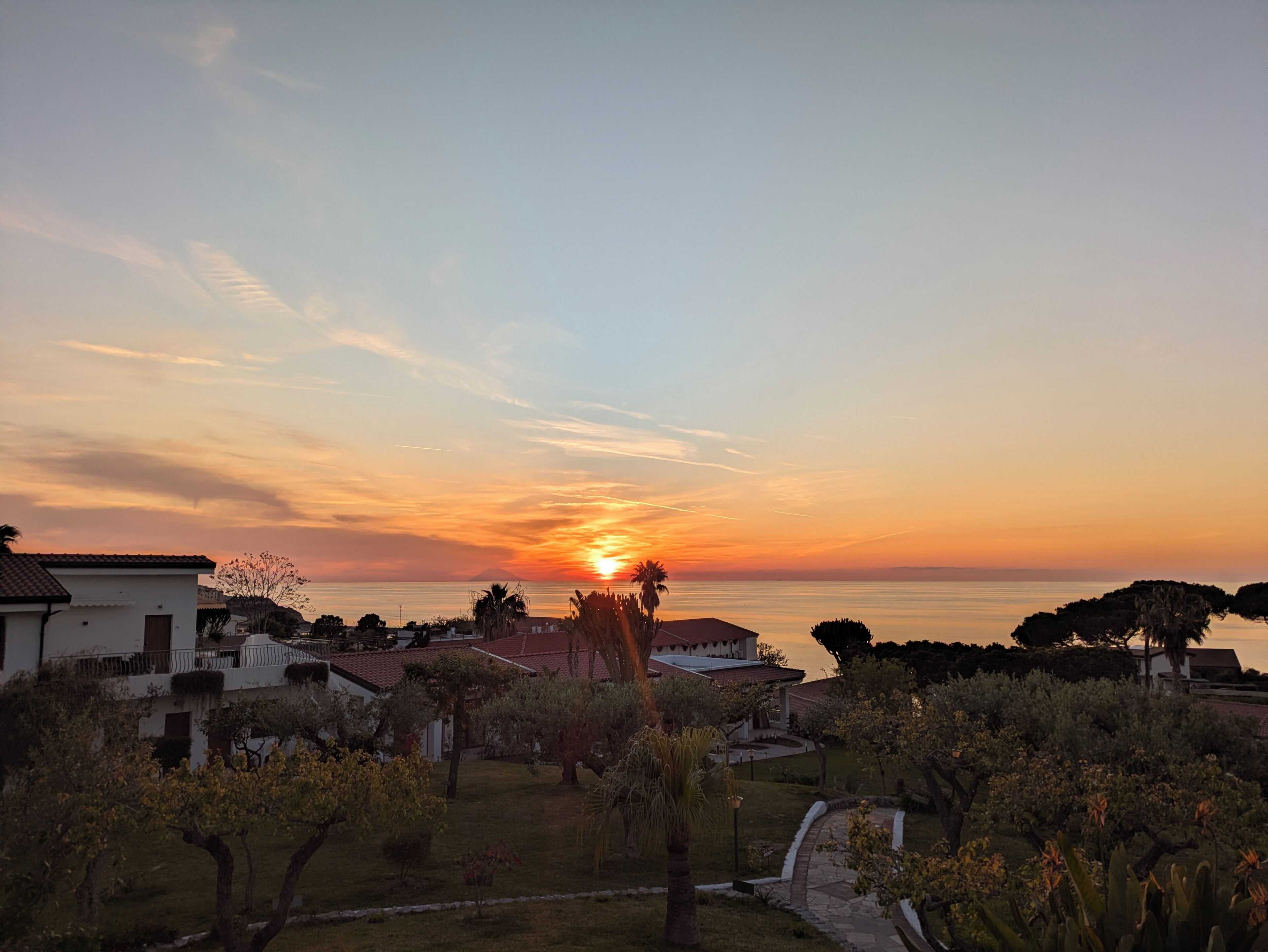 Un coucher de soleil sur une zone résidentielle, avec des maisons et un ciel dégagé.