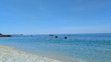 A beach with clear water, pebbly shore, and distant rocky outcrops.