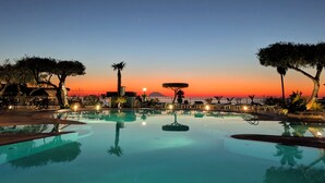 A pool with a sunset view, surrounded by trees and outdoor seating.