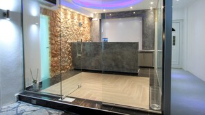 A reception area with a stone wall, a reception desk, and a glass partition. - Gianna Suites (Santorini)