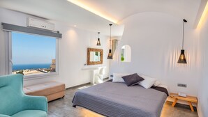 A modern bedroom with a large bed, a view of the sea, a sofa, and pendant lights. - Gianna Suites (Santorini)