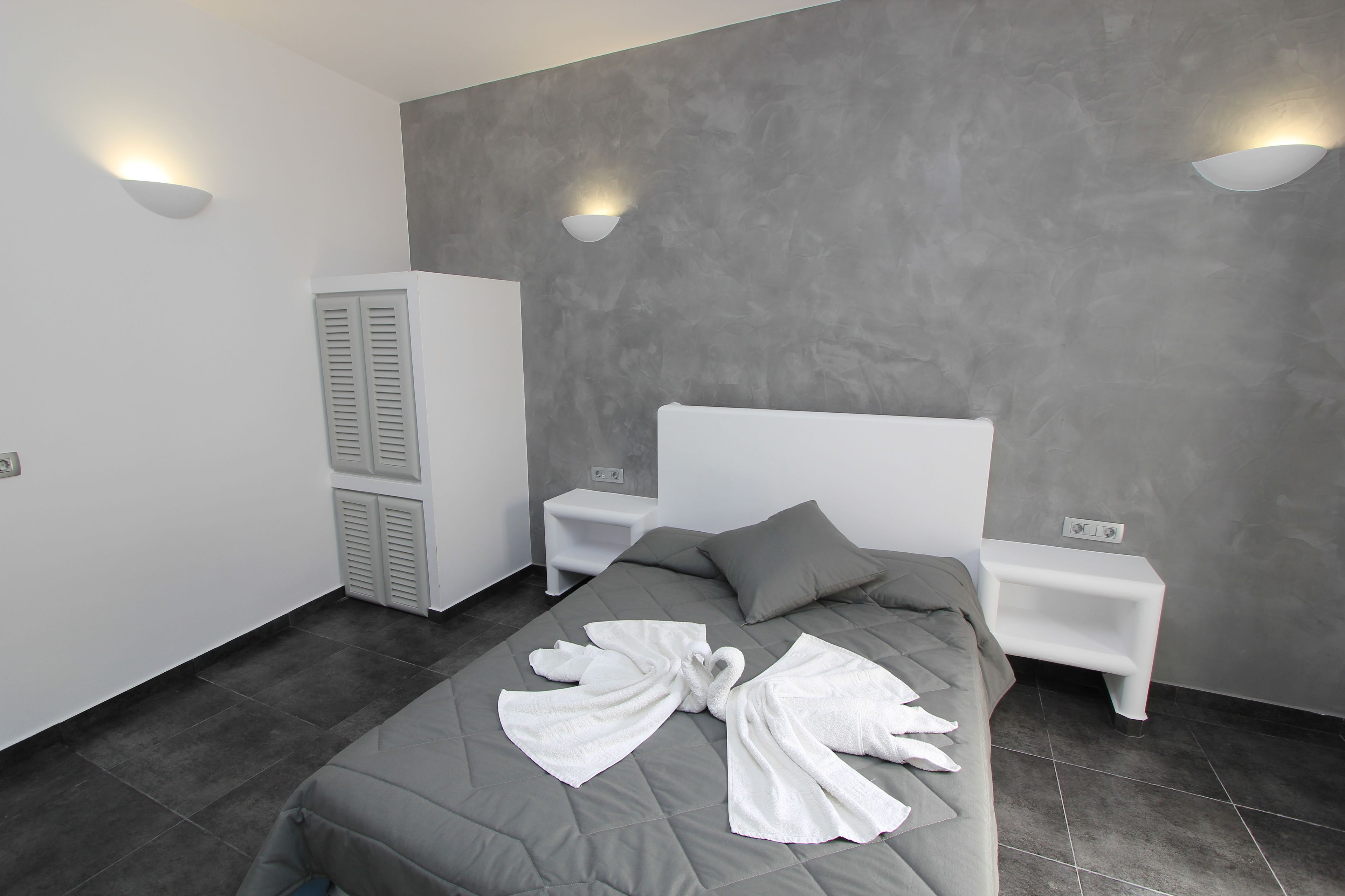 A modern bedroom with a grey bed, white nightstands, and a grey wardrobe.