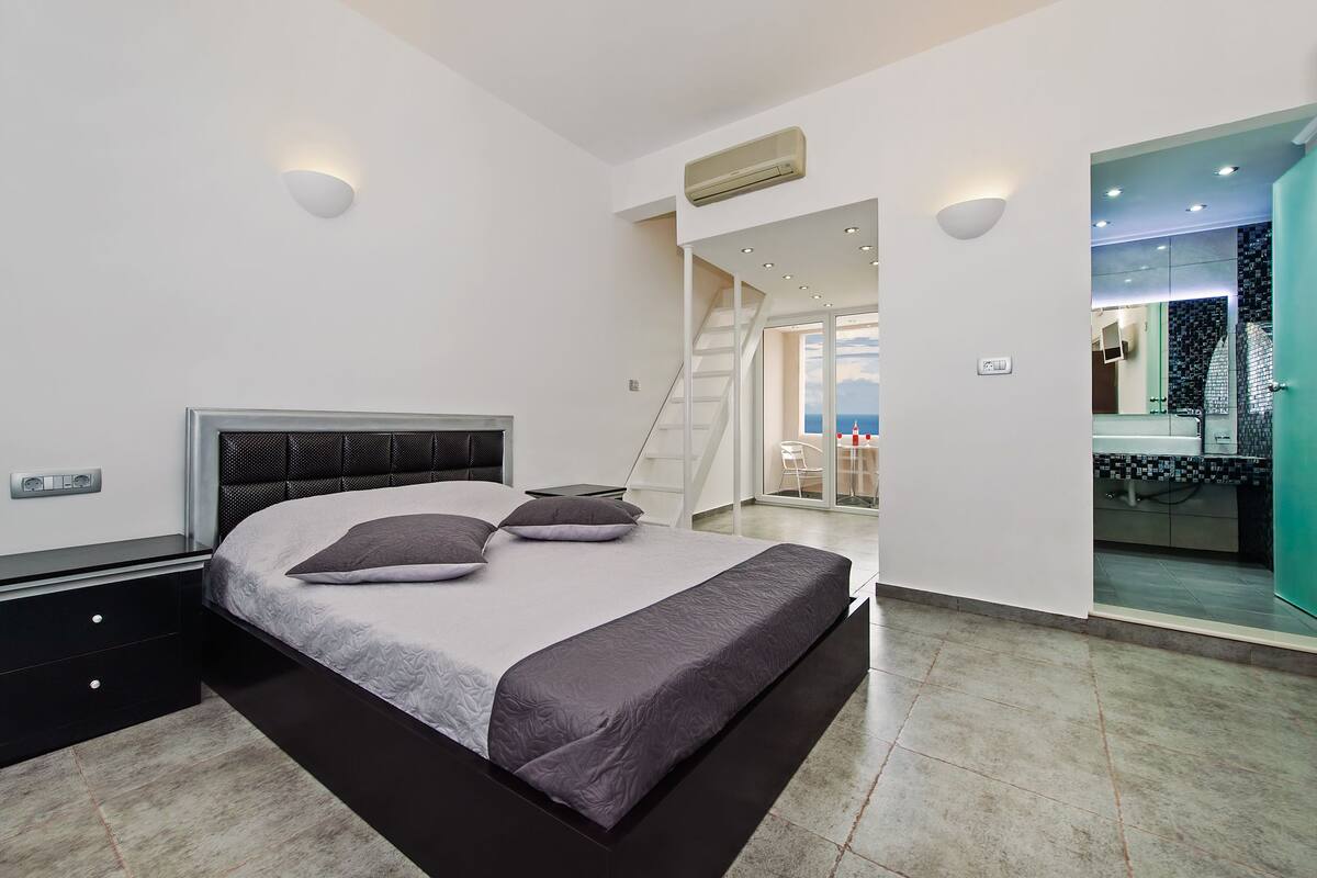 Un dormitorio moderno con una cama grande, una mesita de noche, un calentador incorporado y vistas al baño a través de una puerta de cristal.