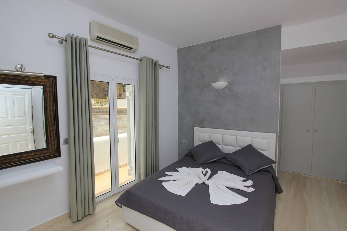 Un dormitorio con cama, espejo, ventana con cortinas y un equipo de aire acondicionado.