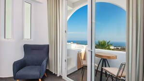A balcony with a view of the sea, a blue armchair, and a table with chairs. - Gianna Suites (Santorini)
