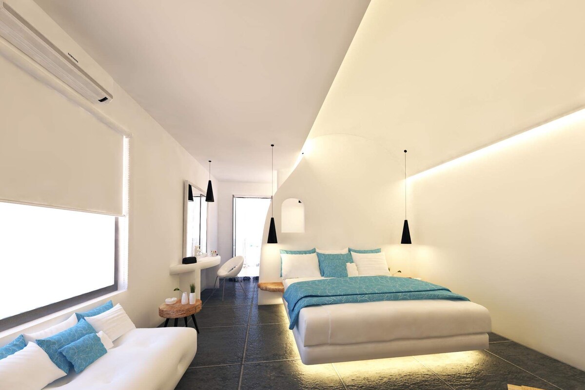 Habitación de hotel moderna con una cama grande, un sofá más pequeño, un tocador con espejo y una mesita de noche con artículos de aseo.