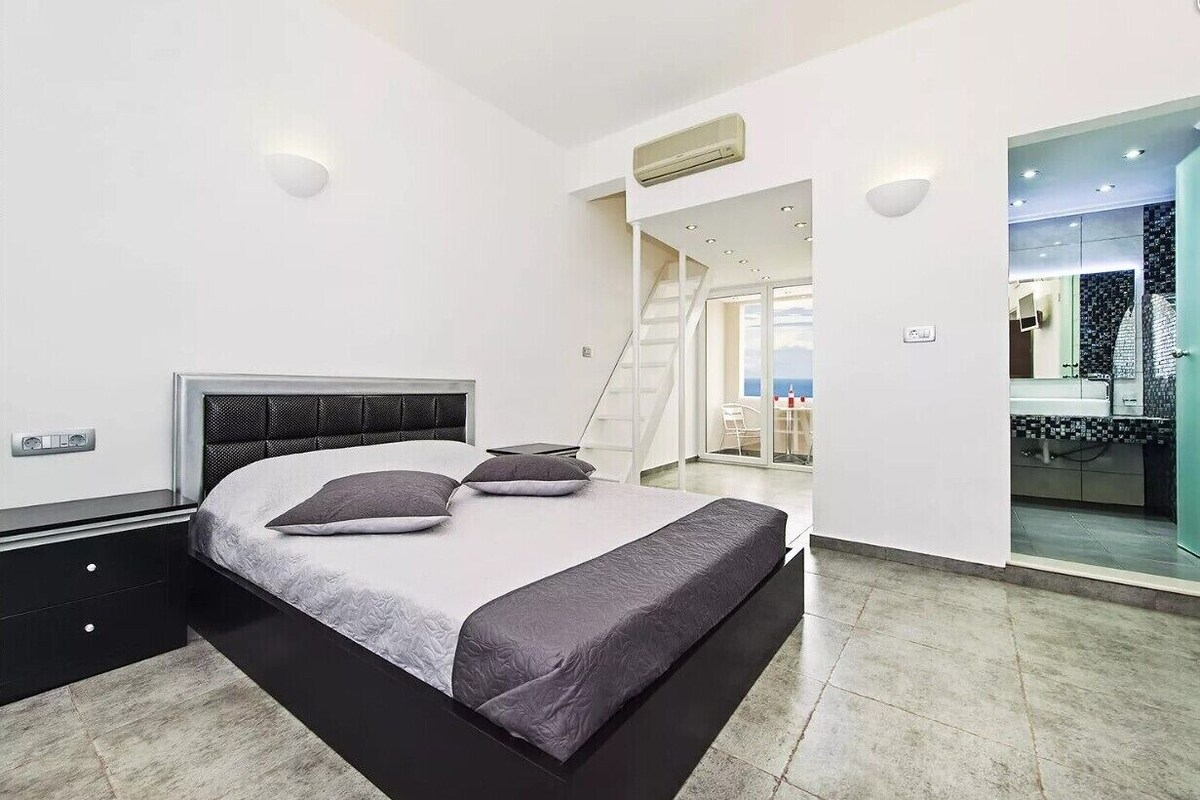 Un dormitorio moderno con cama, mesitas de noche, armario empotrado y una escalera que sube a un nivel superior.
