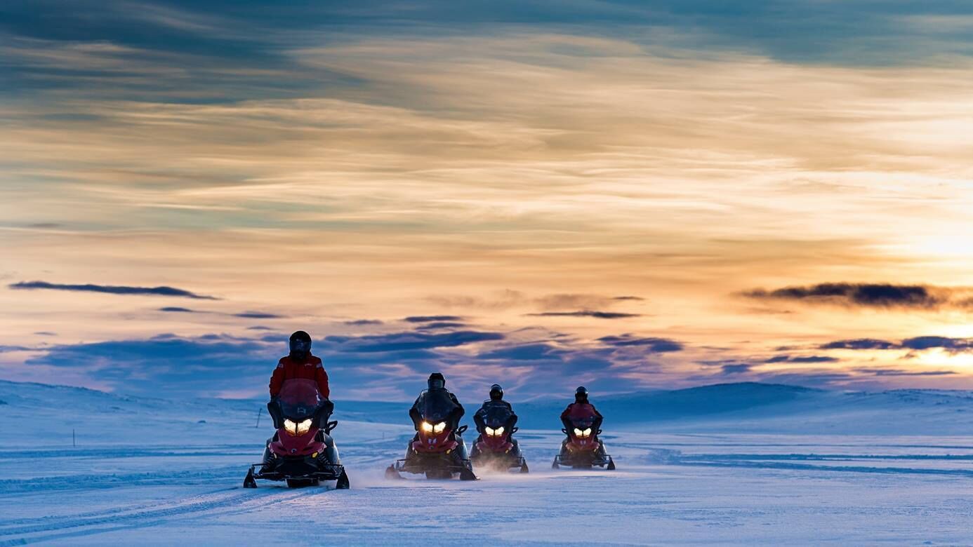 Four snowmobiles on a snowy landscape during sunset.