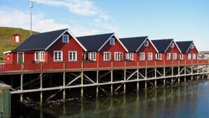 Eine Reihe roter Holzhäuser mit weißen Verzierungen, verbunden durch einen Holzsteg über dem Wasser.