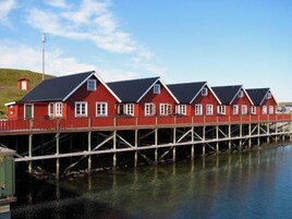 A row of red wooden houses with white trim, connected by a wooden walkway over water.