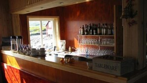 Eine Bar mit einer Holztheke, einem Fenster und Regalen voller Flaschen und Gläser.