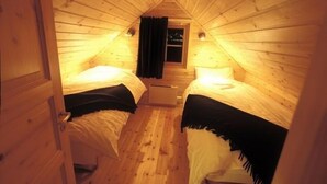 Ein gemütliches Schlafzimmer im Dachgeschoss mit zwei Betten, Holzwänden und einem kleinen Fenster mit Vorhängen.