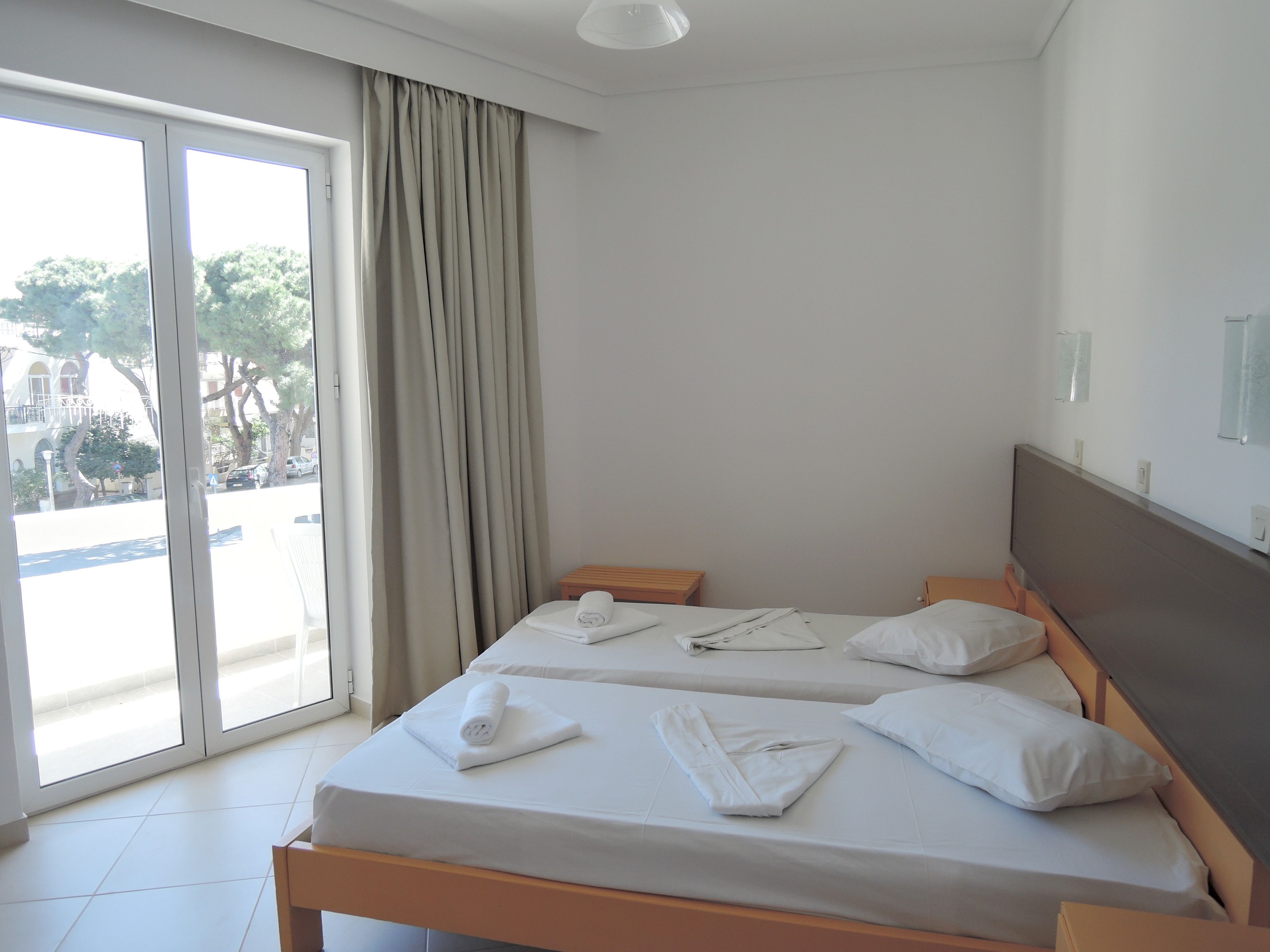 A hotel room with two beds, a sliding glass door to the outside, and a view of the street and trees.