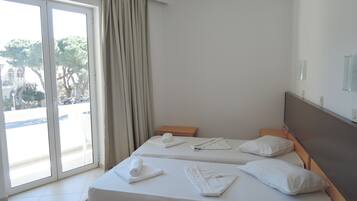 A hotel room with two beds, a sliding glass door to the outside, and a view of the street and trees.