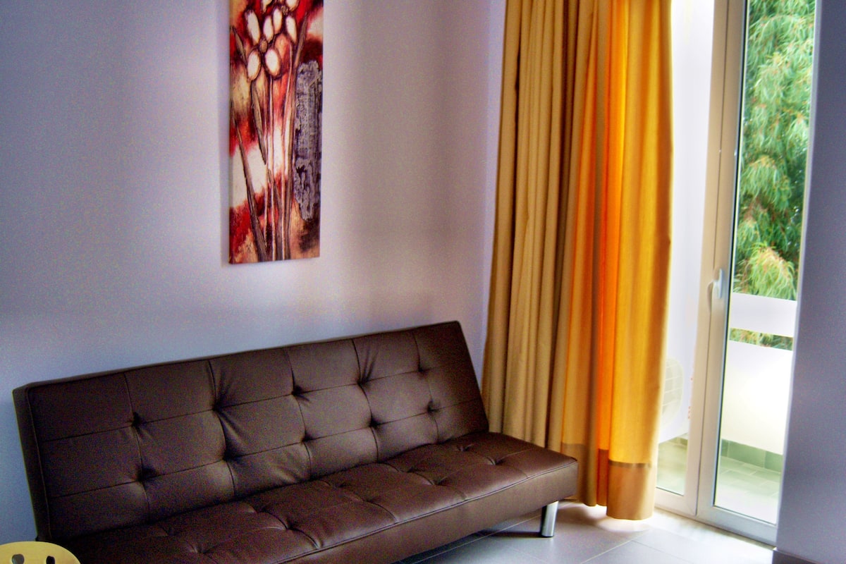 Un salon moderne avec un canapé marron, un tableau au mur et une porte-fenêtre coulissante avec des rideaux.