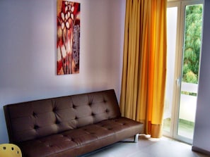Ein modernes Wohnzimmer mit einem braunen Sofa, einem Bild an der Wand und einer Schiebeglastür mit Vorhängen.