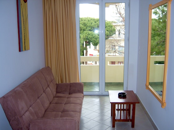 Ein Wohnzimmer mit einer Couch, einem kleinen Tisch und einer Schiebetür zu einem Balkon.