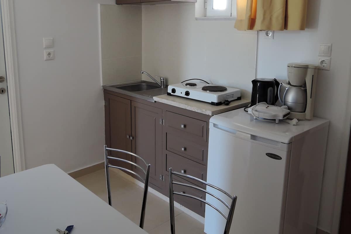 Une cuisine compacte avec un réfrigérateur blanc, une machine à café et un four à micro-ondes posés sur le plan de travail. On y trouve deux chaises et une petite table.