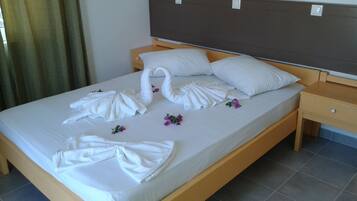 A neatly made bed with towels arranged in swan shapes and a few purple flowers on the bed.