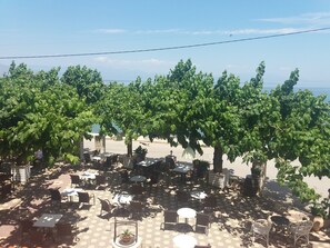An outdoor seating area with tables and chairs, surrounded by lush green trees. - Hotel Panorama (Aigialeia)