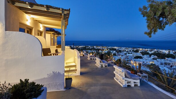 A seaside hotel with a terrace overlooking the ocean, featuring outdoor seating and a view of the coastal town. - Acropole Sunrise (Santorini)