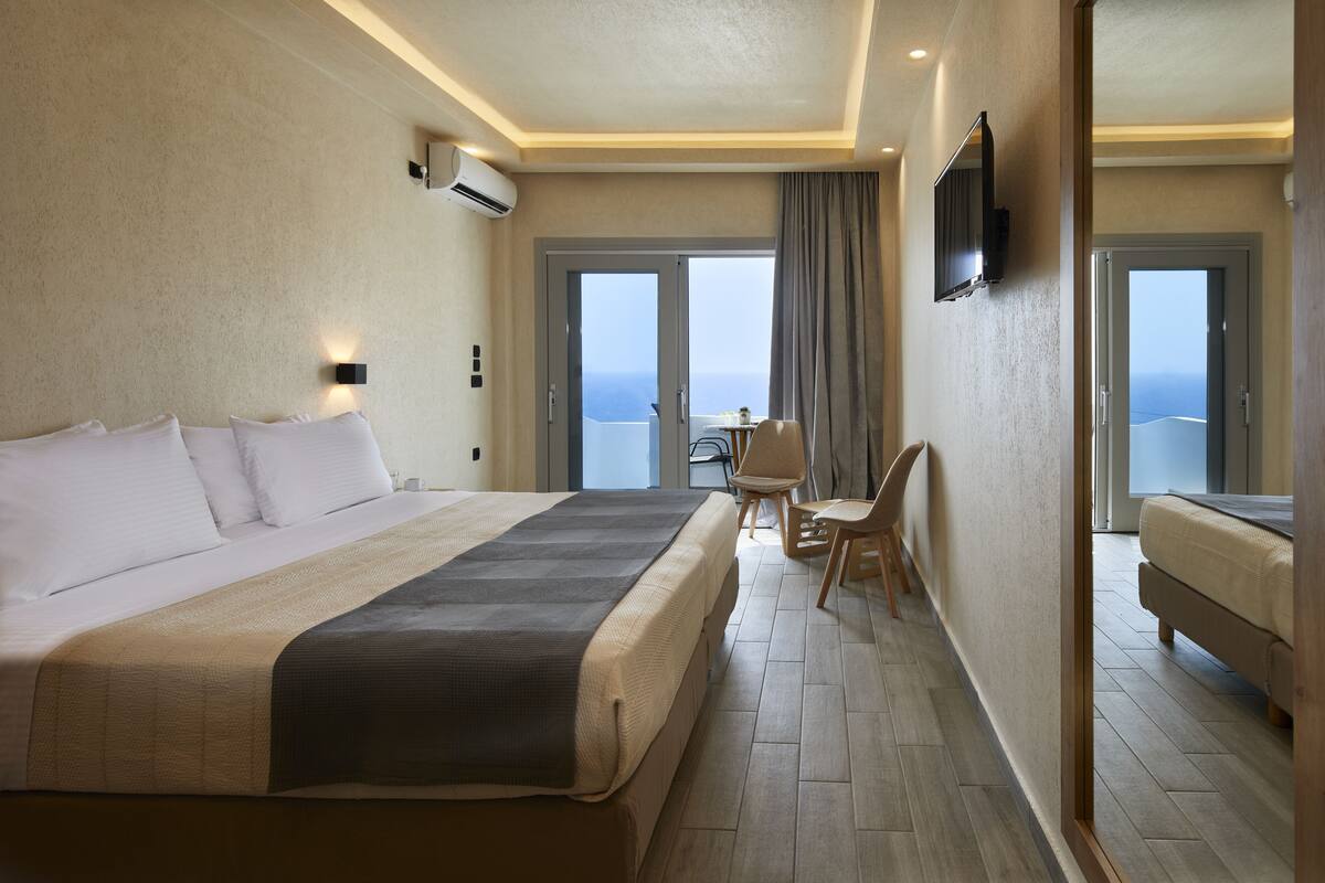 A hotel room with a large bed, a desk, and a chair, a television, and a view of the sea.