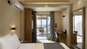A hotel room with a bed, a desk, a chair, and a view of the sea. - Acropole Sunrise (Santorini)