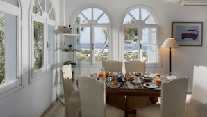 A dining area with a table set for breakfast, overlooking a scenic coastal view. - Acropole Sunrise (Santorini)