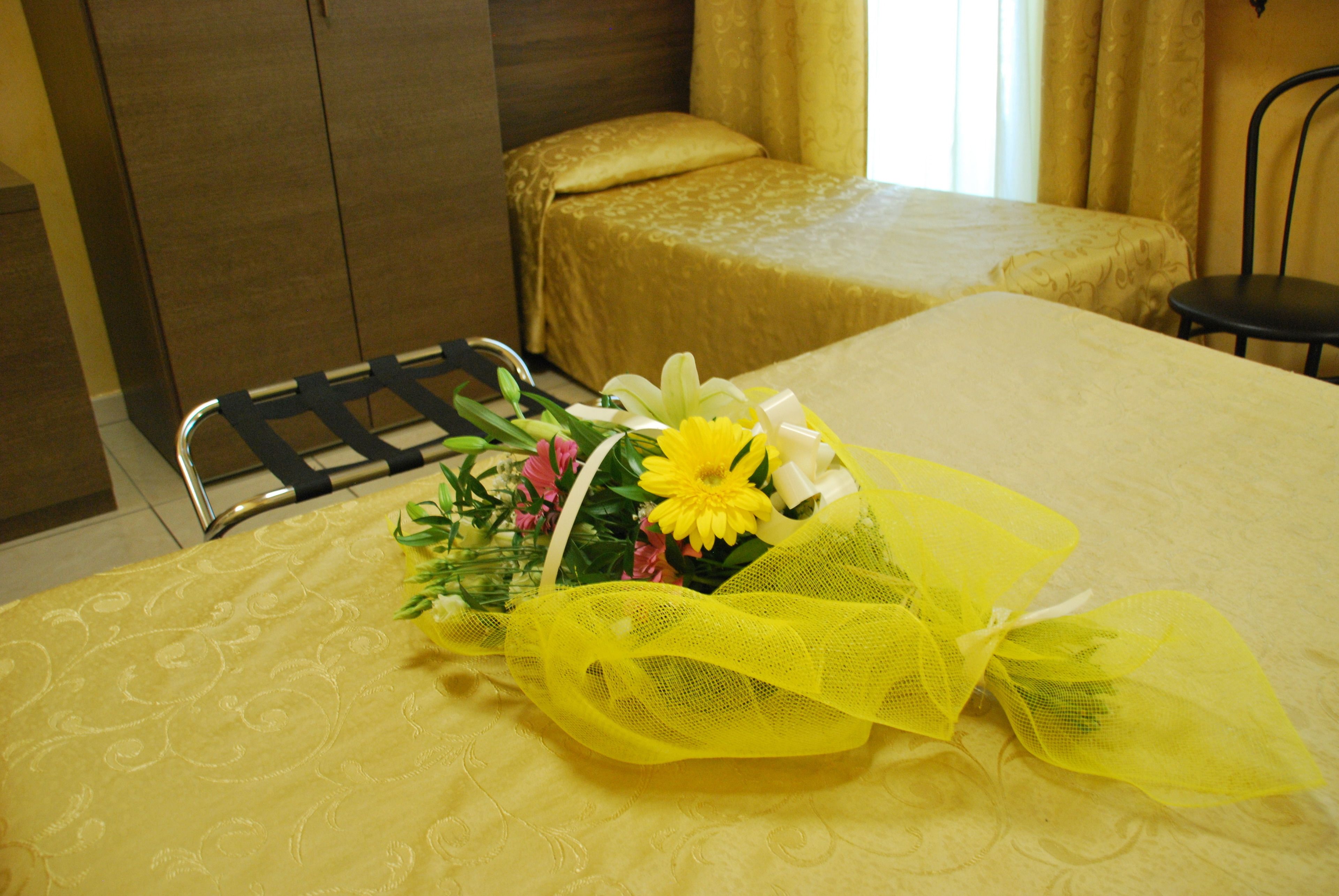 A hotel room with a bed, a small table, and a chair. There is a bouquet of flowers on the bed.