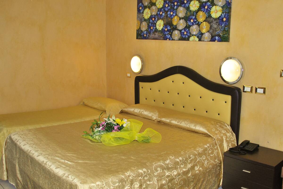 A hotel room with two beds, a floral painting on the wall, bedside lamps, and a telephone on a bedside table.