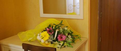 A small desk with a mirror, a chair, and a bouquet of flowers.