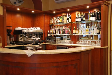 A bar area with a wooden counter, espresso machine, and shelves of liquor bottles.