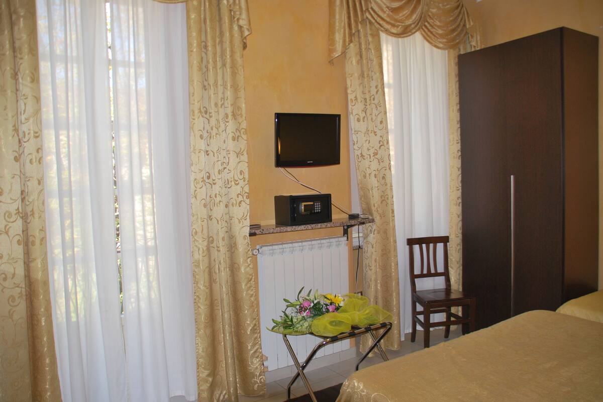 A hotel room with a bed, a chair, a television mounted on the wall, and a small table with flowers.