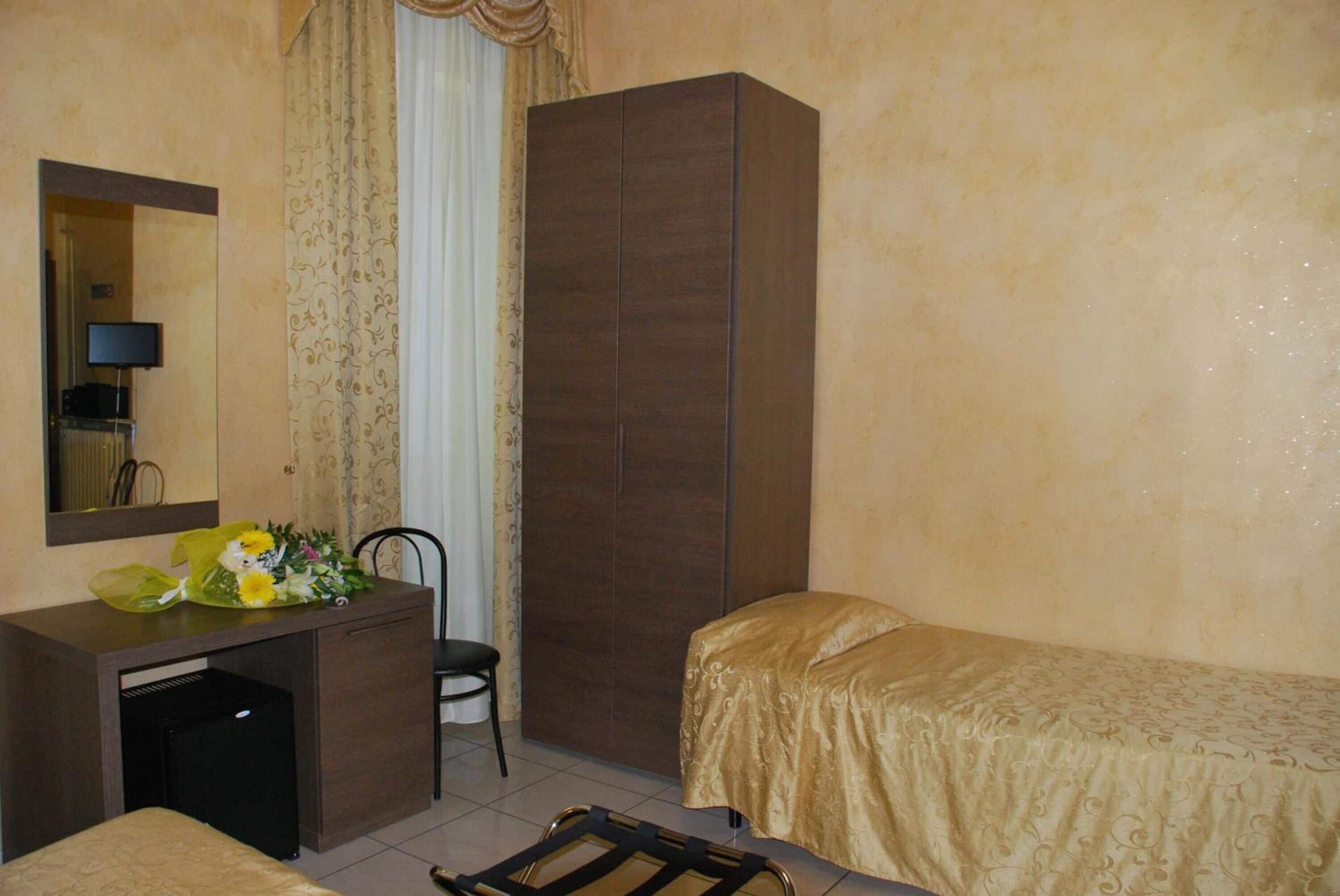 A hotel room with a bed, a desk with a mirror, a wardrobe, and a chair.