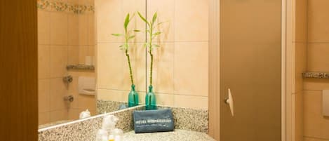 Un baño con encimera de granito, un espejo, un lavabo, dos plantas de bambú y un perchero para toallas.