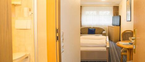 A hotel room with a bed, a small desk, a chair, a television, and a bathroom with a toilet and sink.