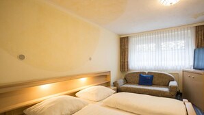 Una habitación de hotel con dos camas, un sofá, un televisor y una ventana con cortinas.