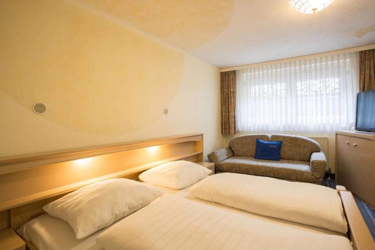 A hotel room with two beds, a sofa, a TV, and a window with curtains.