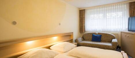 Ein Hotelzimmer mit zwei Betten, einem Sofa, einem Fernseher und einem Fenster mit Vorhängen.
