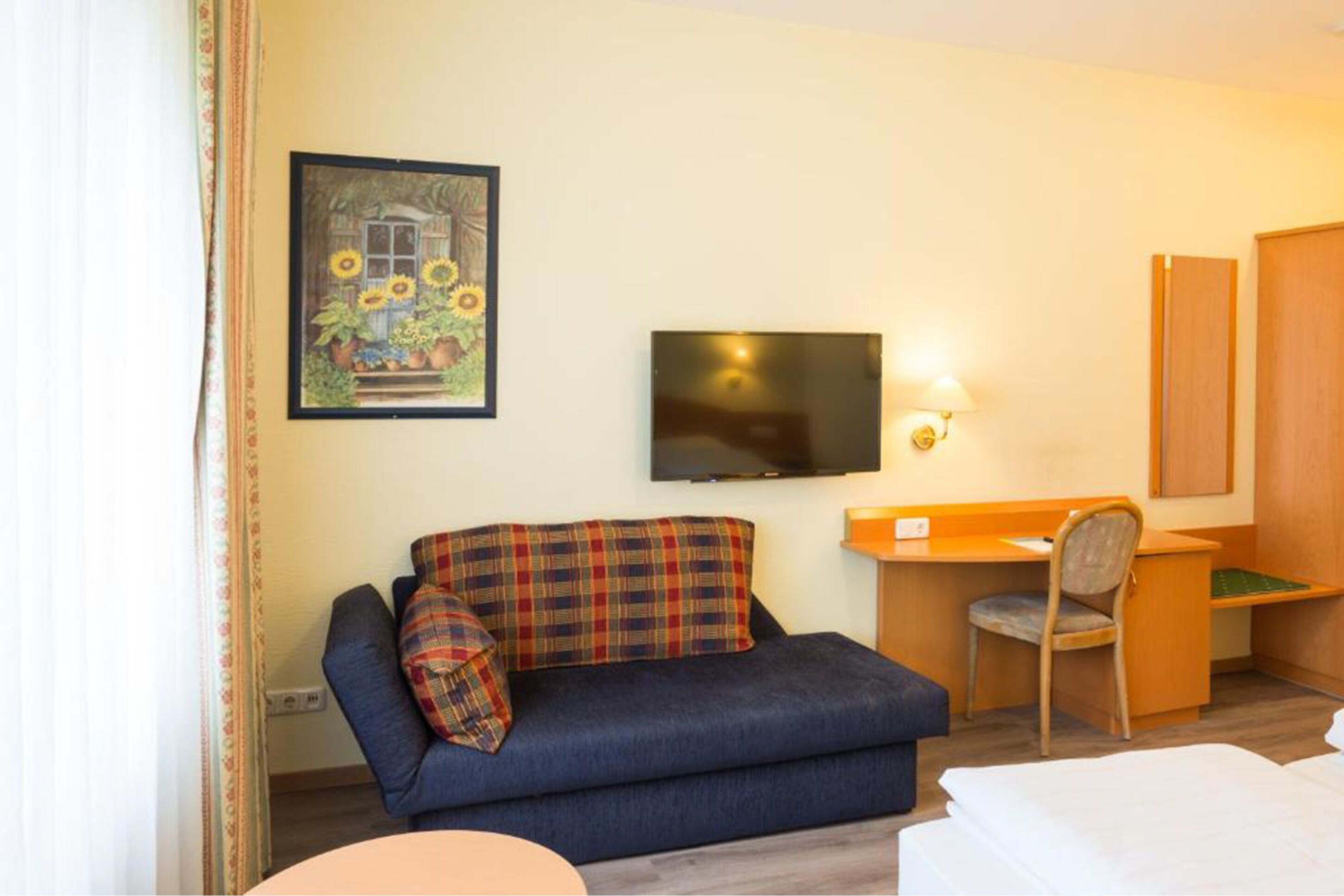 A hotel room with a sofa, a desk, a chair, a TV, and a bed.