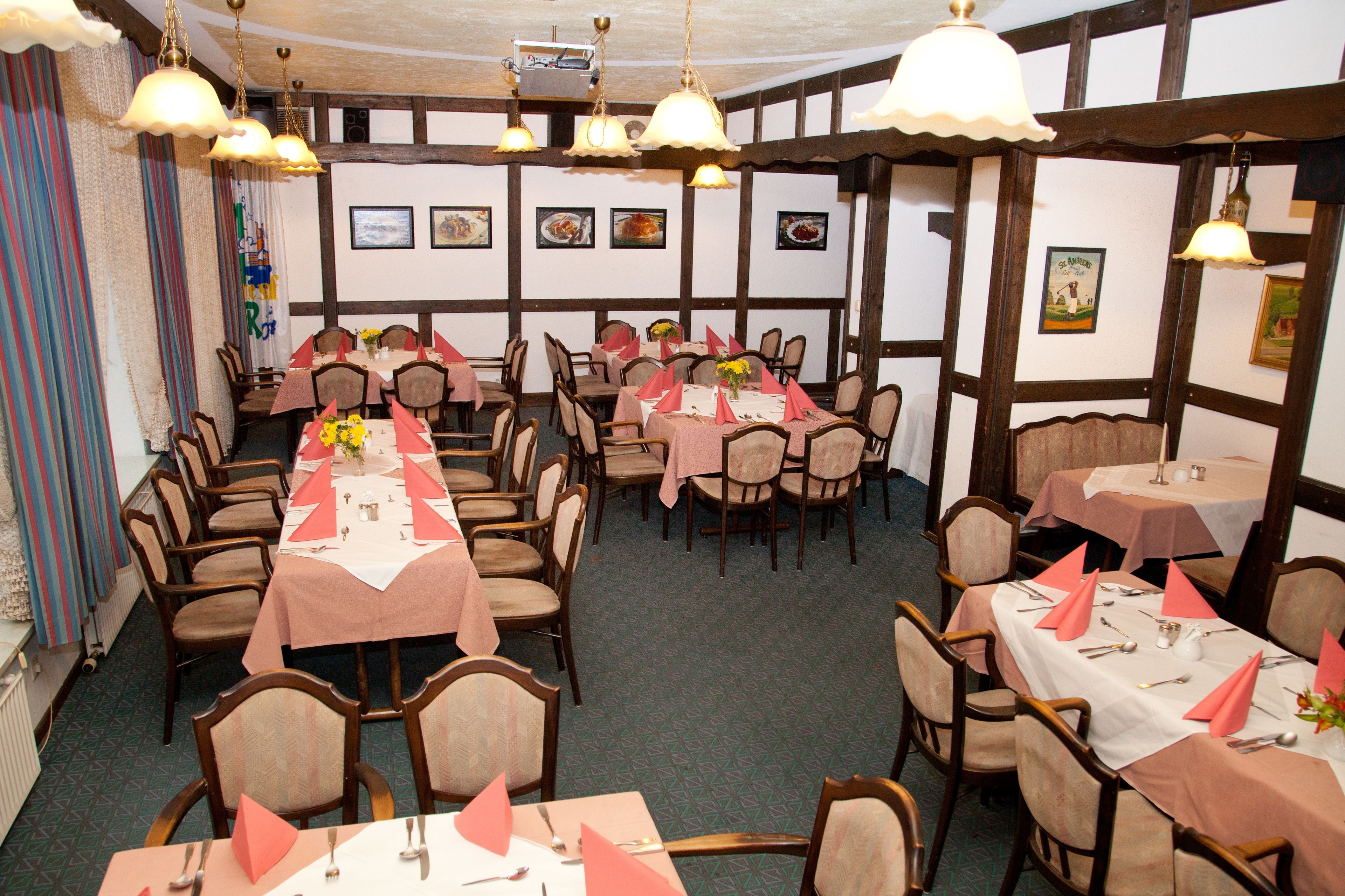 A dining area with multiple tables set for service, featuring a traditional European style with exposed wooden beams and hanging light fixtures.