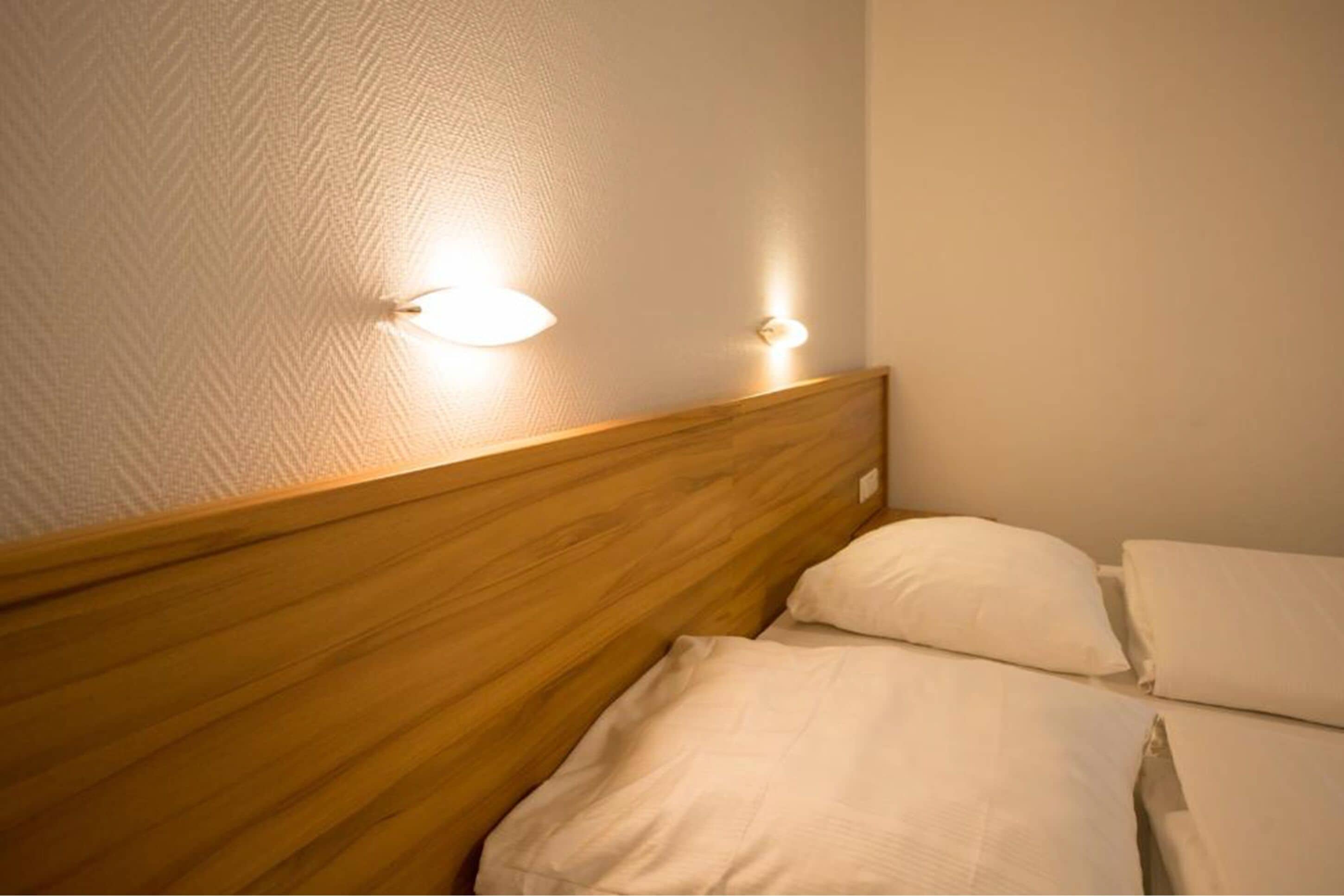 A neatly made bed with a wooden headboard and two wall-mounted lights.