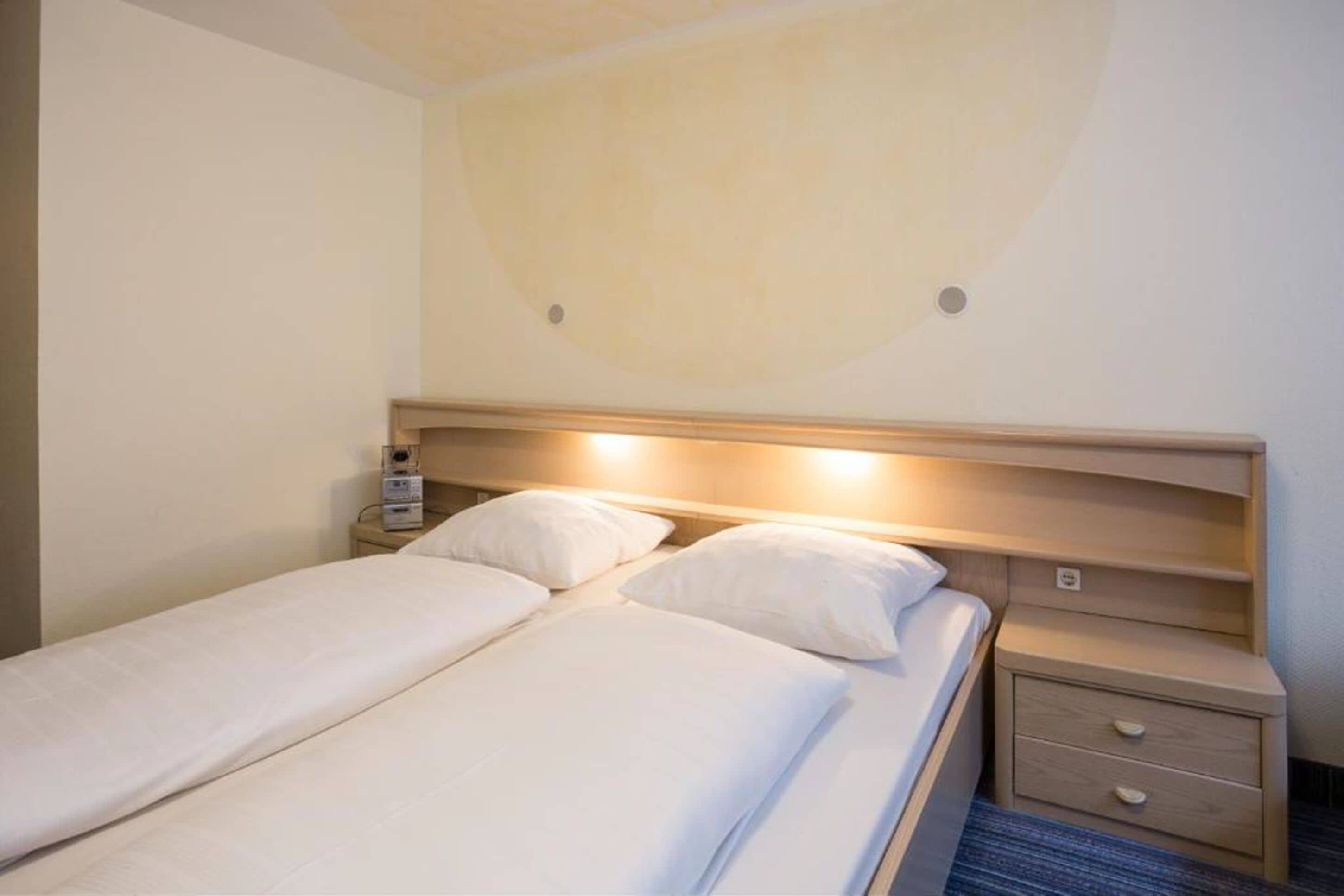 Een tweepersoonsbed met witte lakens, een houten hoofdbord en nachtkastjes met lades.