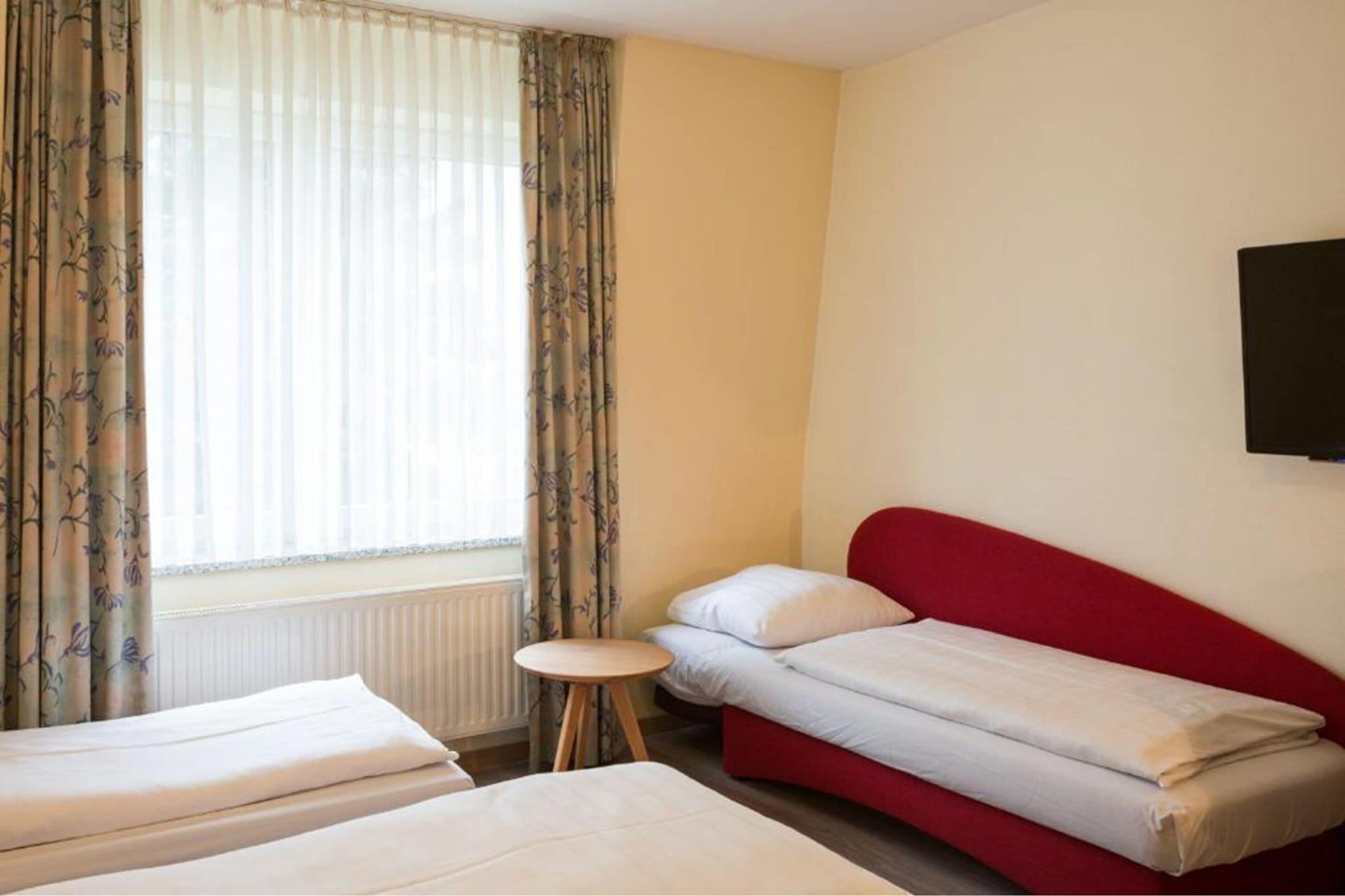 Une chambre d’hôtel avec deux lits, une petite table ronde et une fenêtre avec des rideaux.