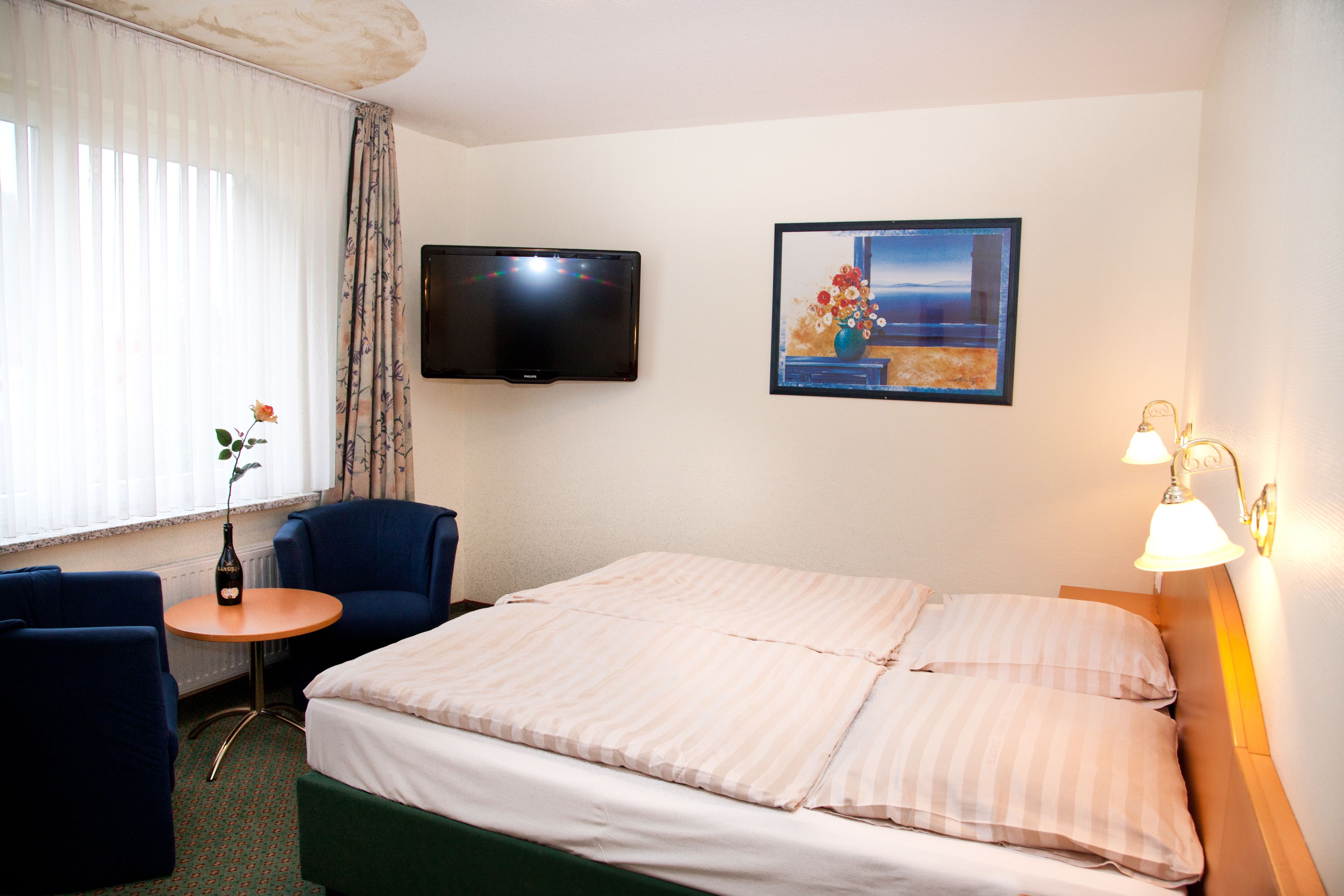 Une chambre d’hôtel avec un lit, une chaise, une petite table, un téléviseur et un tableau au mur.