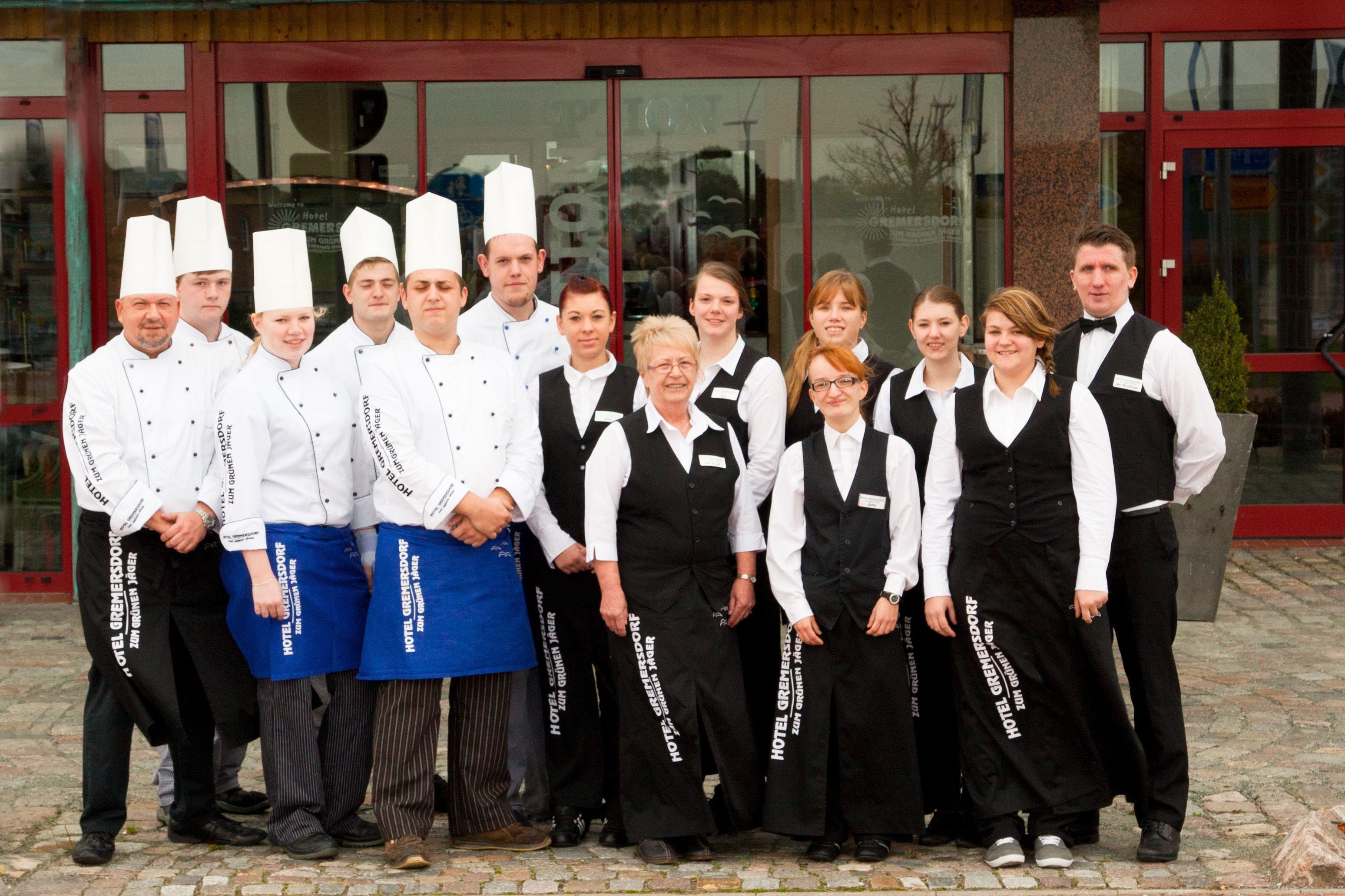 A group of hotel staff in front of a building with large windows and a red door.