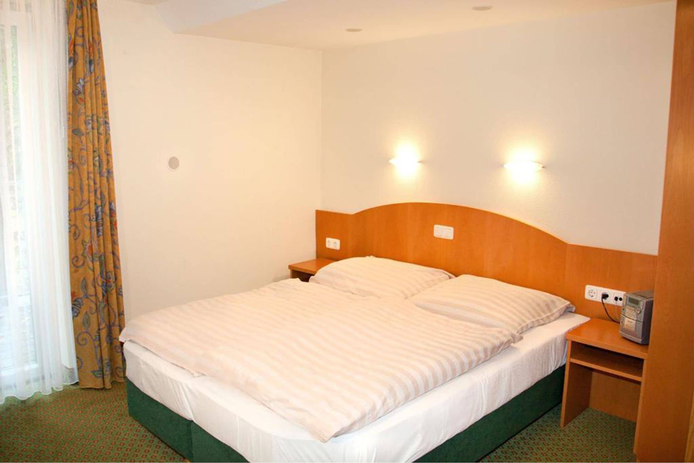Une chambre d’hôtel avec un lit simple, deux tables de chevet, une tête de lit en bois et deux lampes fixées au mur.